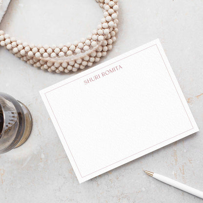 Flat notecard styled with pearl necklace and pencil on light stone surface, name printed in Ironroot red.