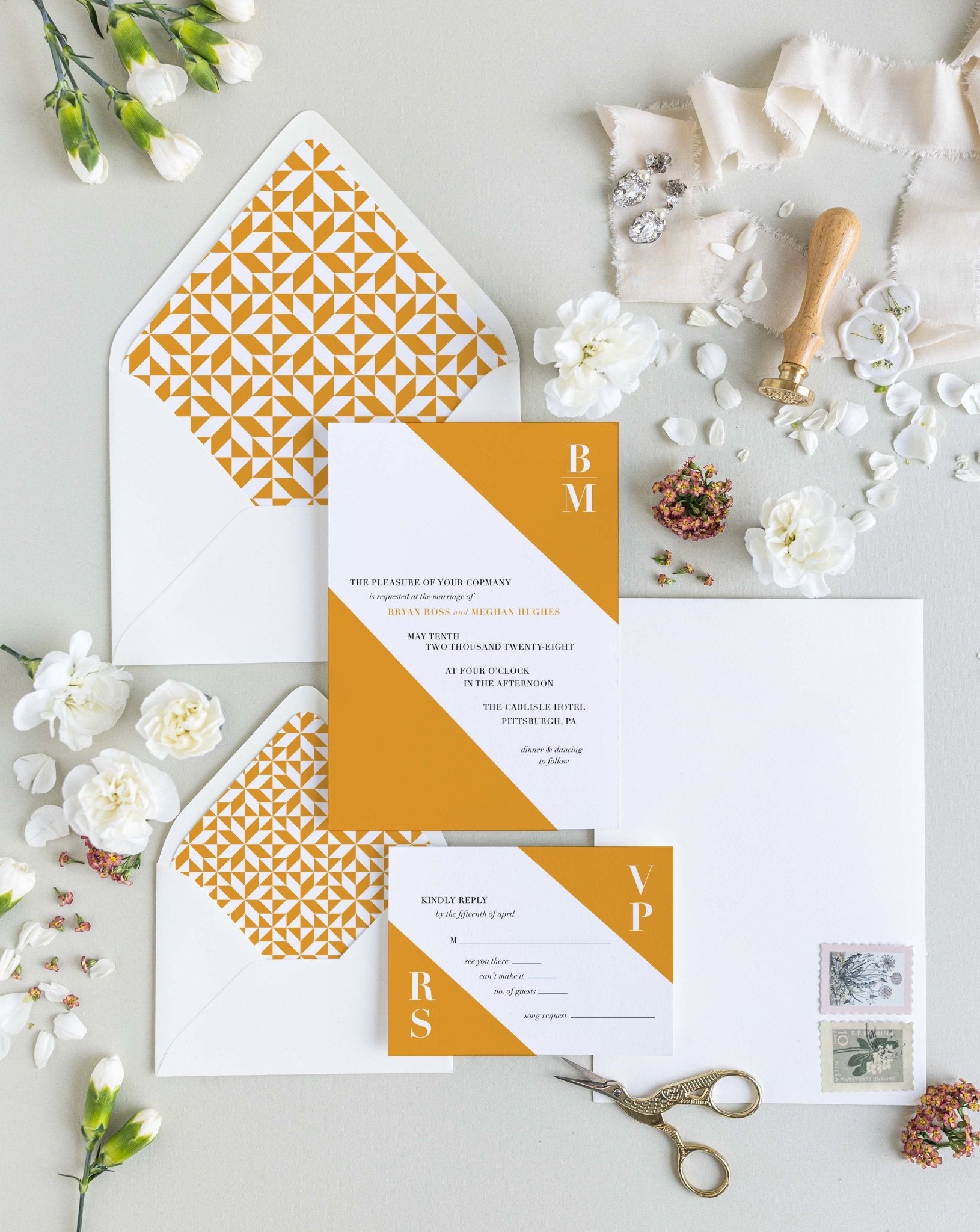 Slanted wedding invitation suite by Blú Rose, invitation and reply card with a diagonal marigold color block and monogram, styled with marigold geometric-lined envelopes, ribbon, and a wax seal