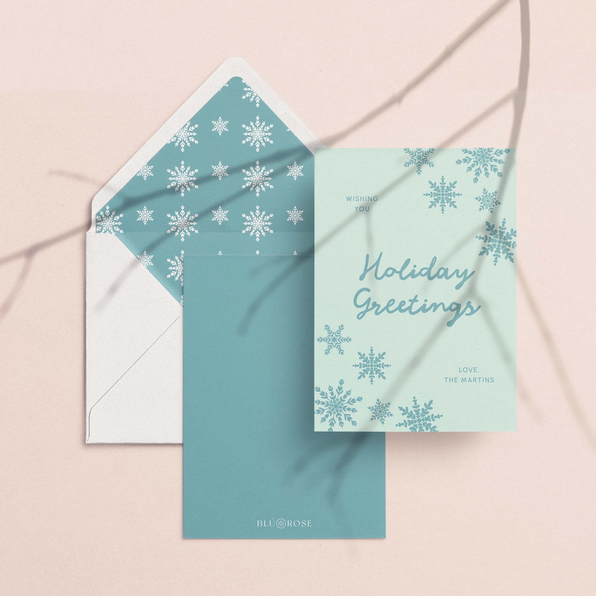 Snowflake Greetings card with its teal snowflake envelope liner styled on a blush backdrop