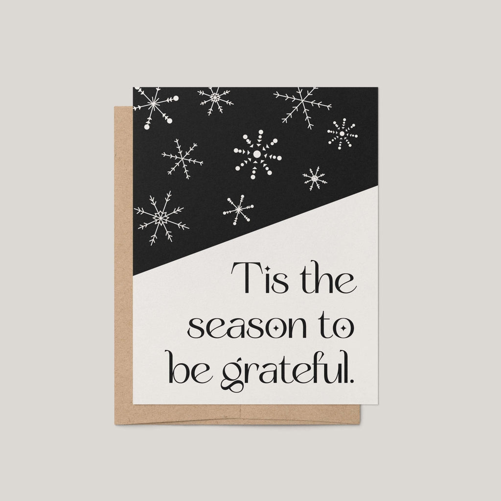 Snowflake Hill holiday greeting card by Blú Rose, black and cream card with white snowflakes and Tis the season to be grateful text, shown with kraft envelope