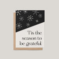 Snowflake Hill holiday greeting card by Blú Rose, black and cream card with white snowflakes and Tis the season to be grateful text, shown with kraft envelope