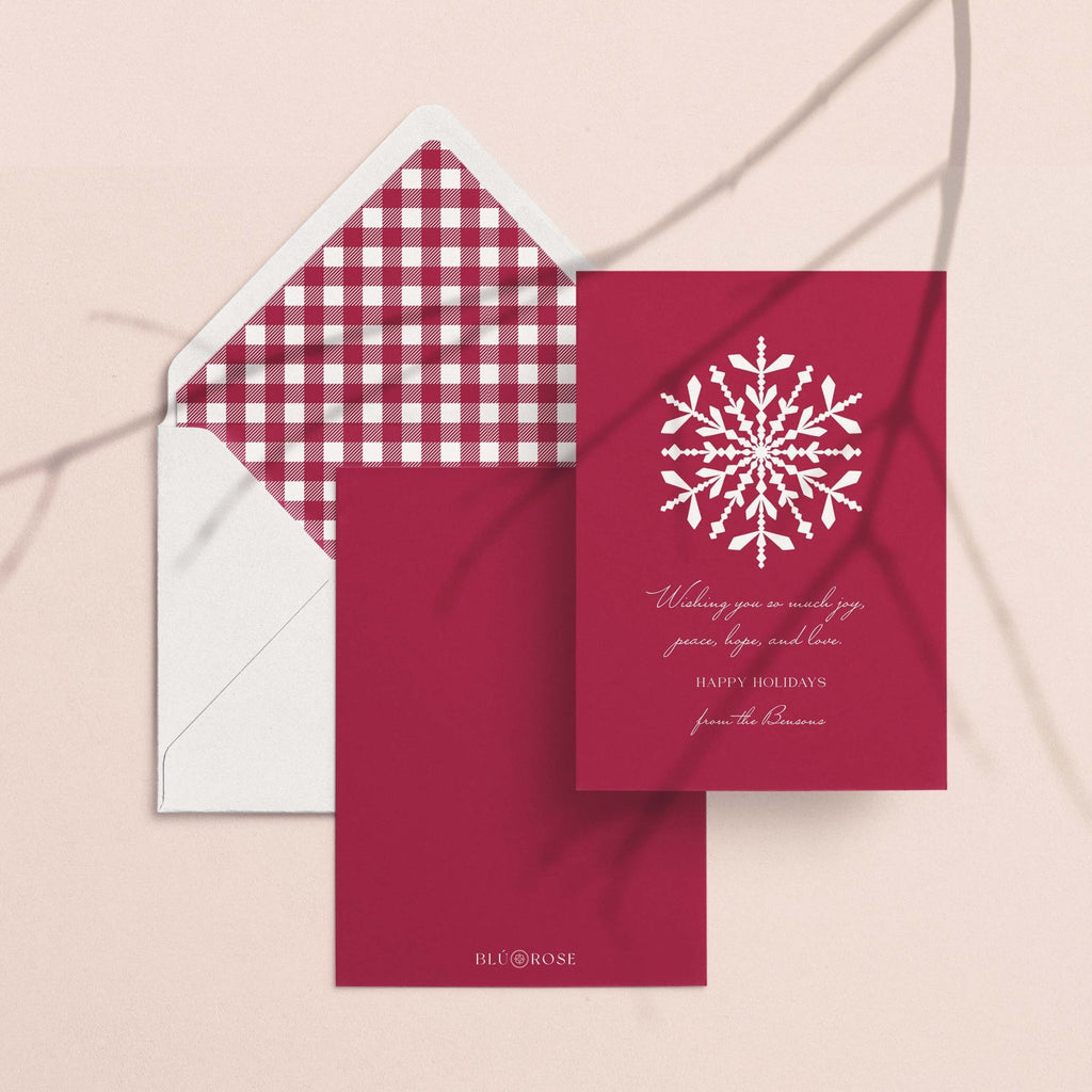 Snowflake card with its burgundy gingham envelope liner styled on a blush backdrop