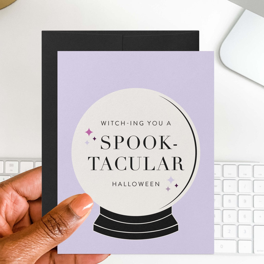 Halloween greeting card with crystal ball design styled on desk with black envelope and computer keyboard.