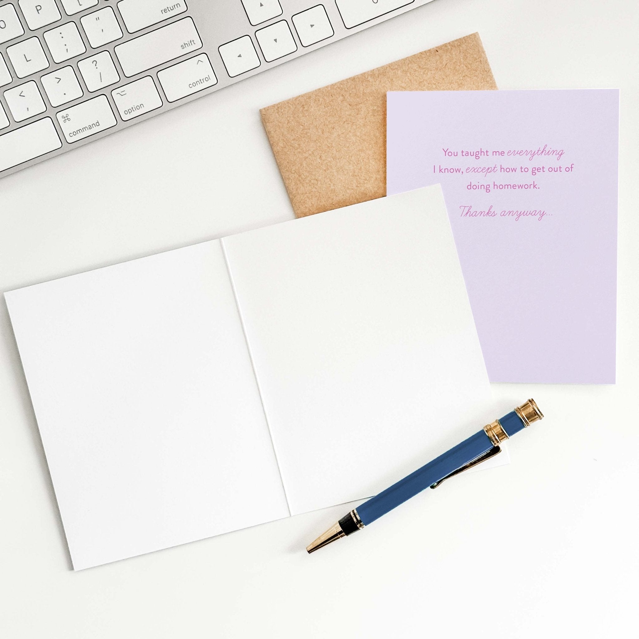 Taught Me Everything teacher card by Blú Rose shown open with blank interior, kraft envelope and pen on a white desk