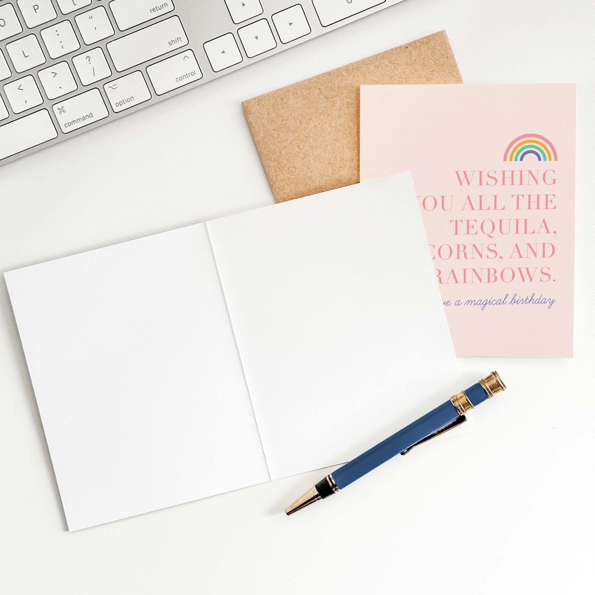 Tequila, Unicorns & Rainbows birthday card by Blú Rose shown open with a blank interior, kraft envelope and pen on a white desk