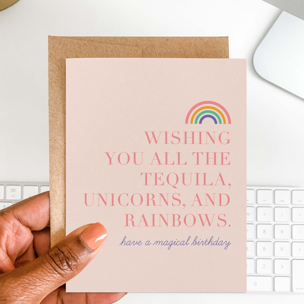 Tequila, Unicorns & Rainbows birthday card by Blú Rose held in hand over a white desk with a keyboard and kraft envelope