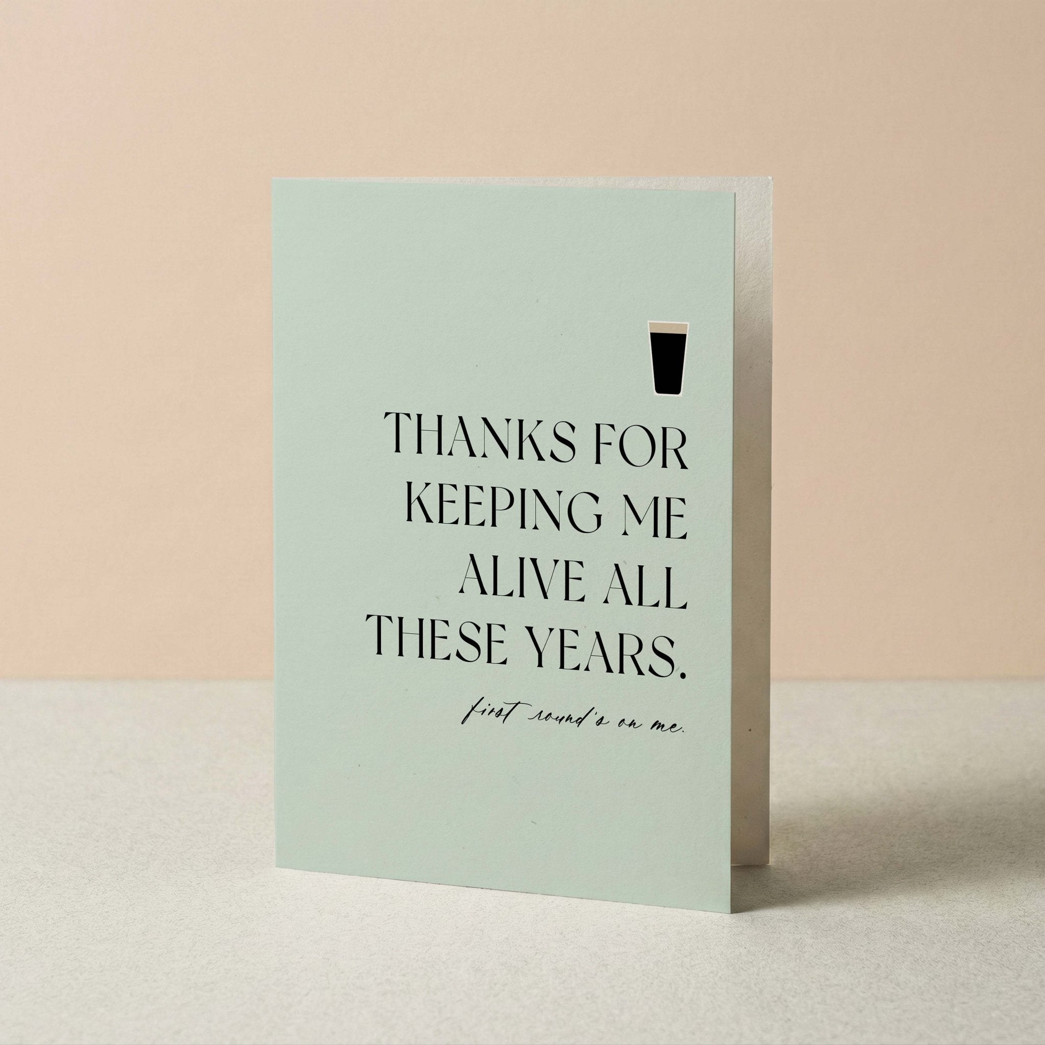 Thanks for Keeping Me Alive funny dad card by Blú Rose standing upright, sage card with beer illustration on a neutral background