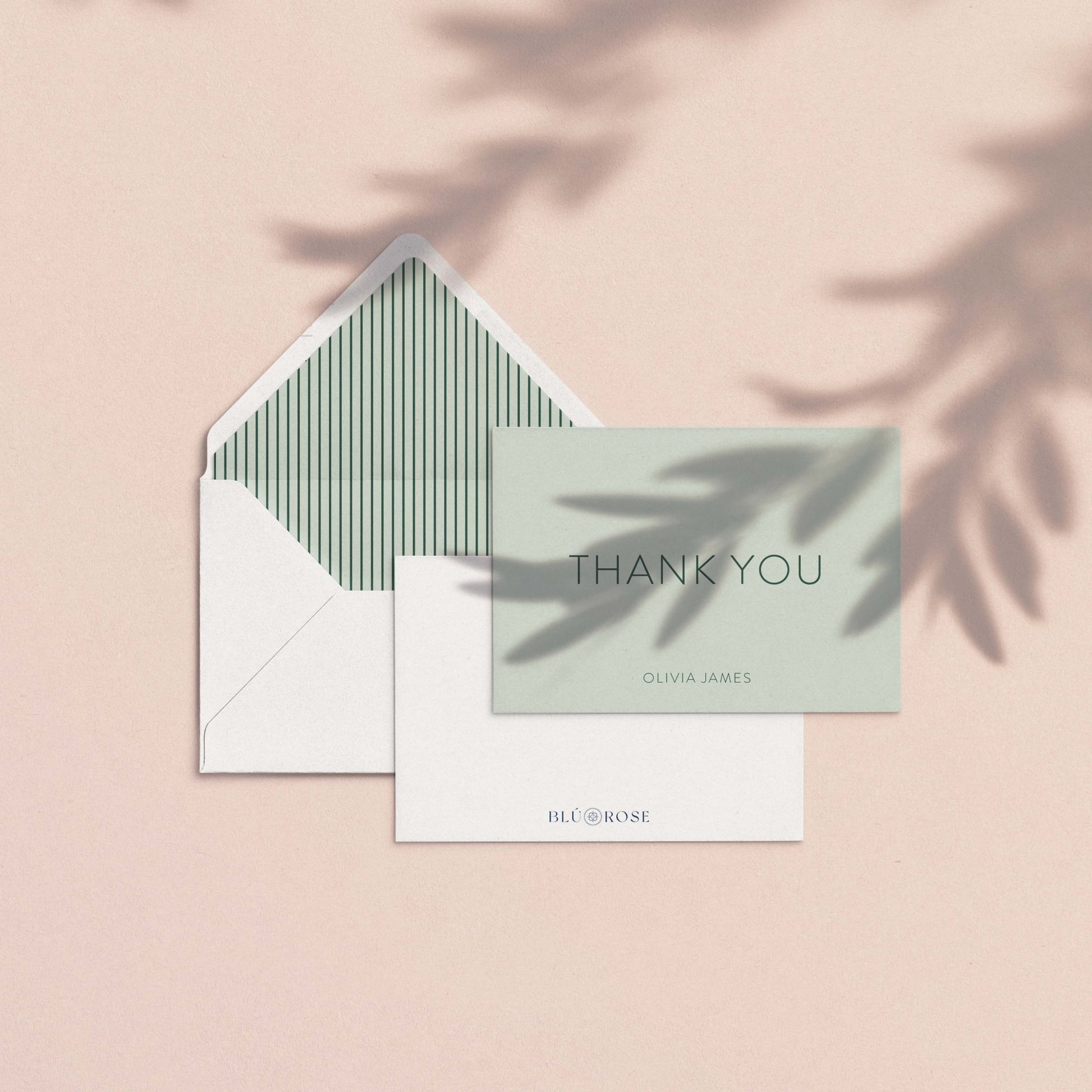 The Olivia thank you card shown with striped envelope liner and white envelope on a blush background with soft botanical shadows