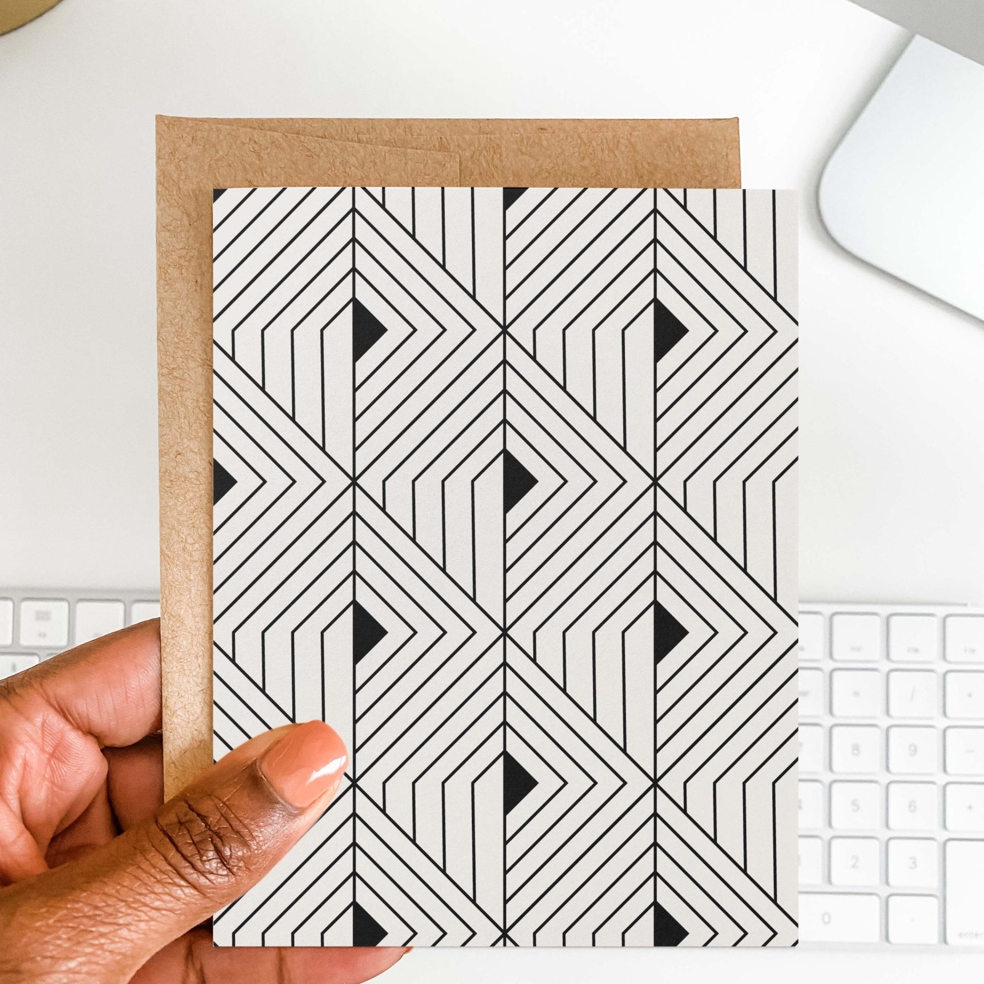 Hand holding The Prism Greeting Card by Blú Rose showing the geometric angular pattern with kraft envelope against a white keyboard