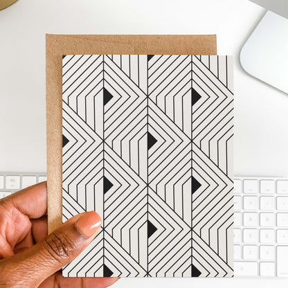 Hand holding The Prism Greeting Card by Blú Rose showing the geometric angular pattern with kraft envelope against a white keyboard