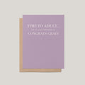 Time to Adult funny graduation greeting card by Blú Rose, lavender card with white serif congrats grad text, shown with kraft envelope