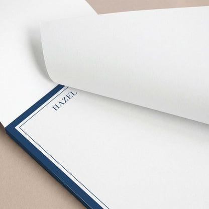 Close-up of personalized navy border notepad with top sheet slightly lifted.