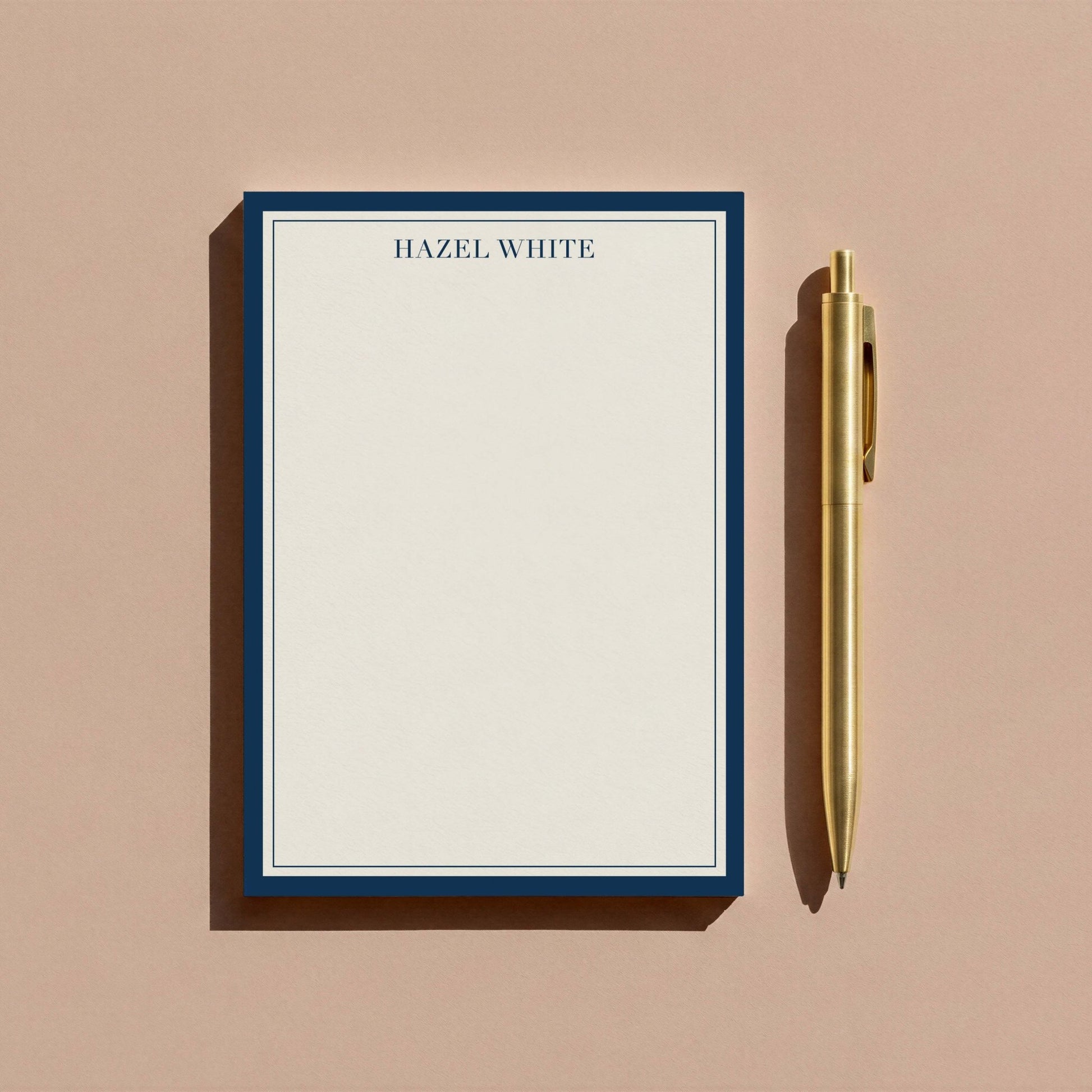 Navy skinny border notepad styled with gold pen on warm tan surface.