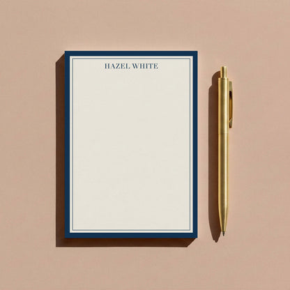 Navy skinny border notepad styled with gold pen on warm tan surface.