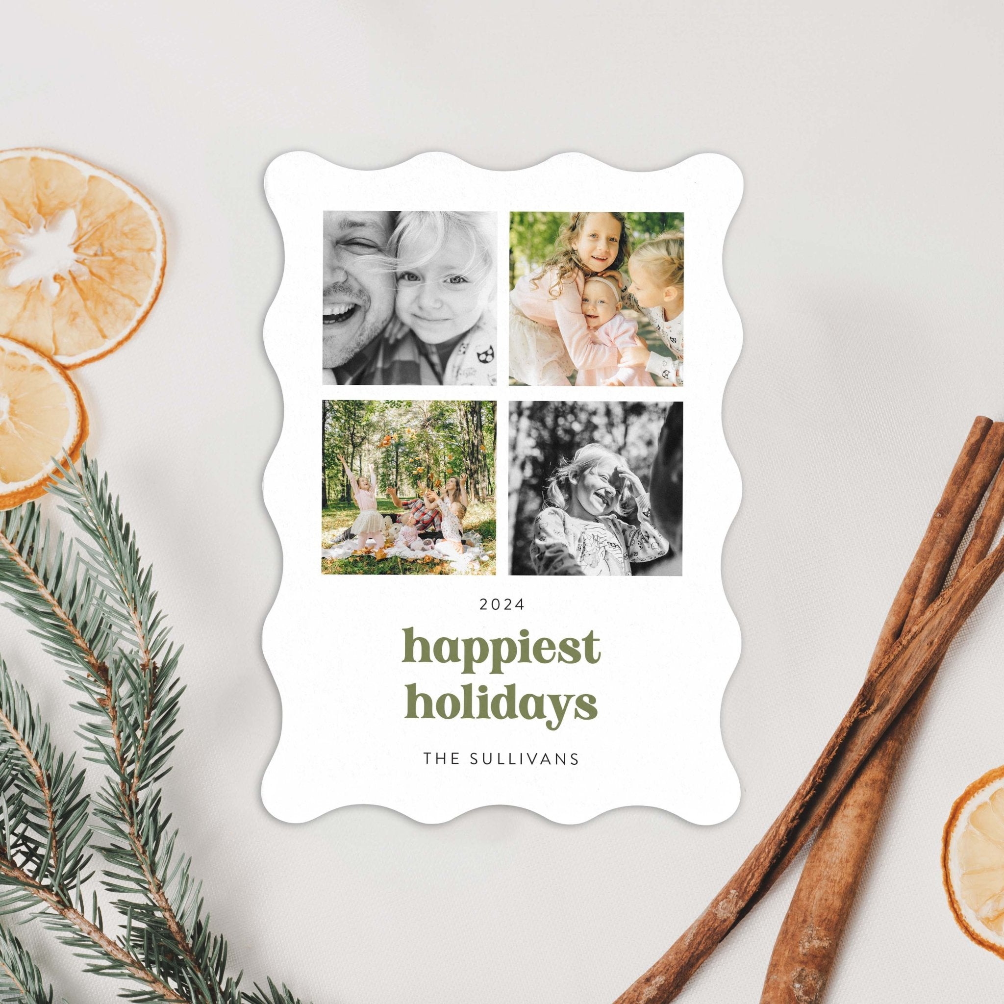 Wavy-edge holiday card displayed in a styled flat lay with winter greenery and dried citrus.