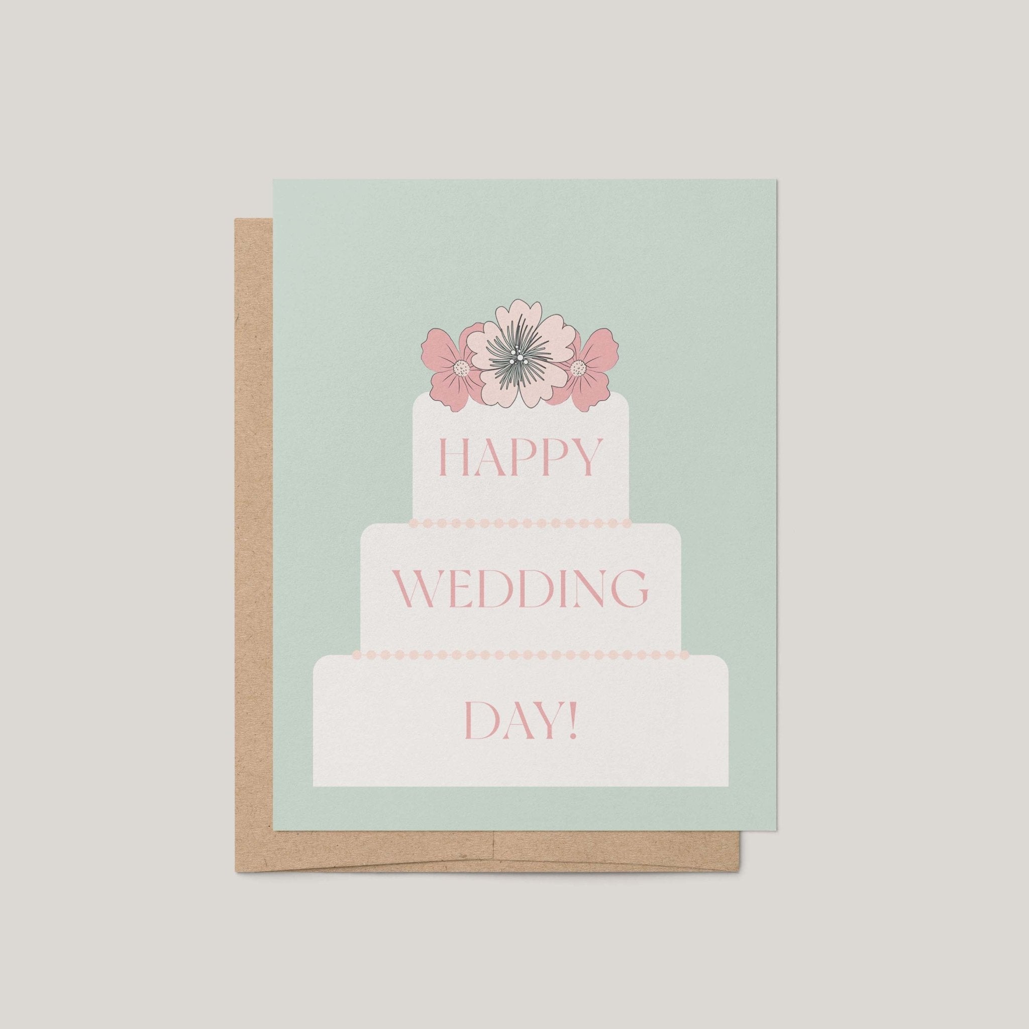 A greeting card with a kraft envelope, featuring a pastel mint background and an illustration of a three-tier wedding cake topped with pink flowers. The words 'HAPPY WEDDING DAY!' are printed on the cake in pink.