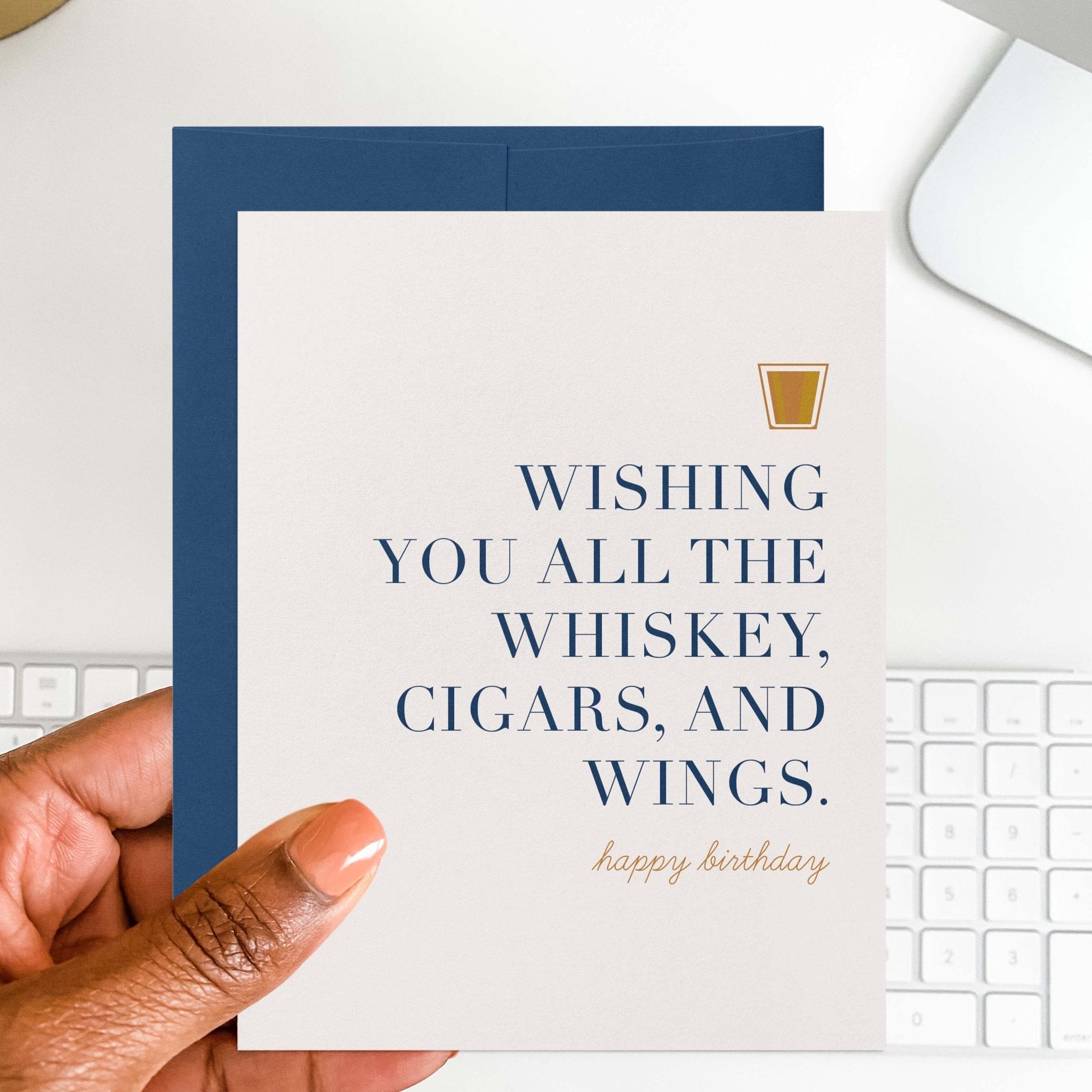Whiskey Birthday card by Blú Rose held in hand over a white desk with keyboard and blue envelope