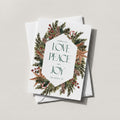 Winter Wreath holiday card with an evergreen, pinecone and berry wreath framing LOVE PEACE and JOY in green lettering