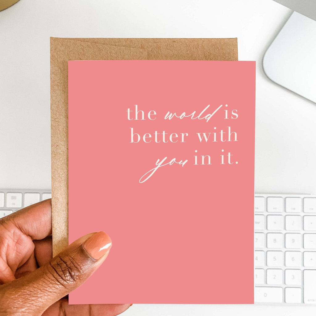 World is Better With You supportive card by Blú Rose held in hand over a white desk with keyboard and kraft envelope