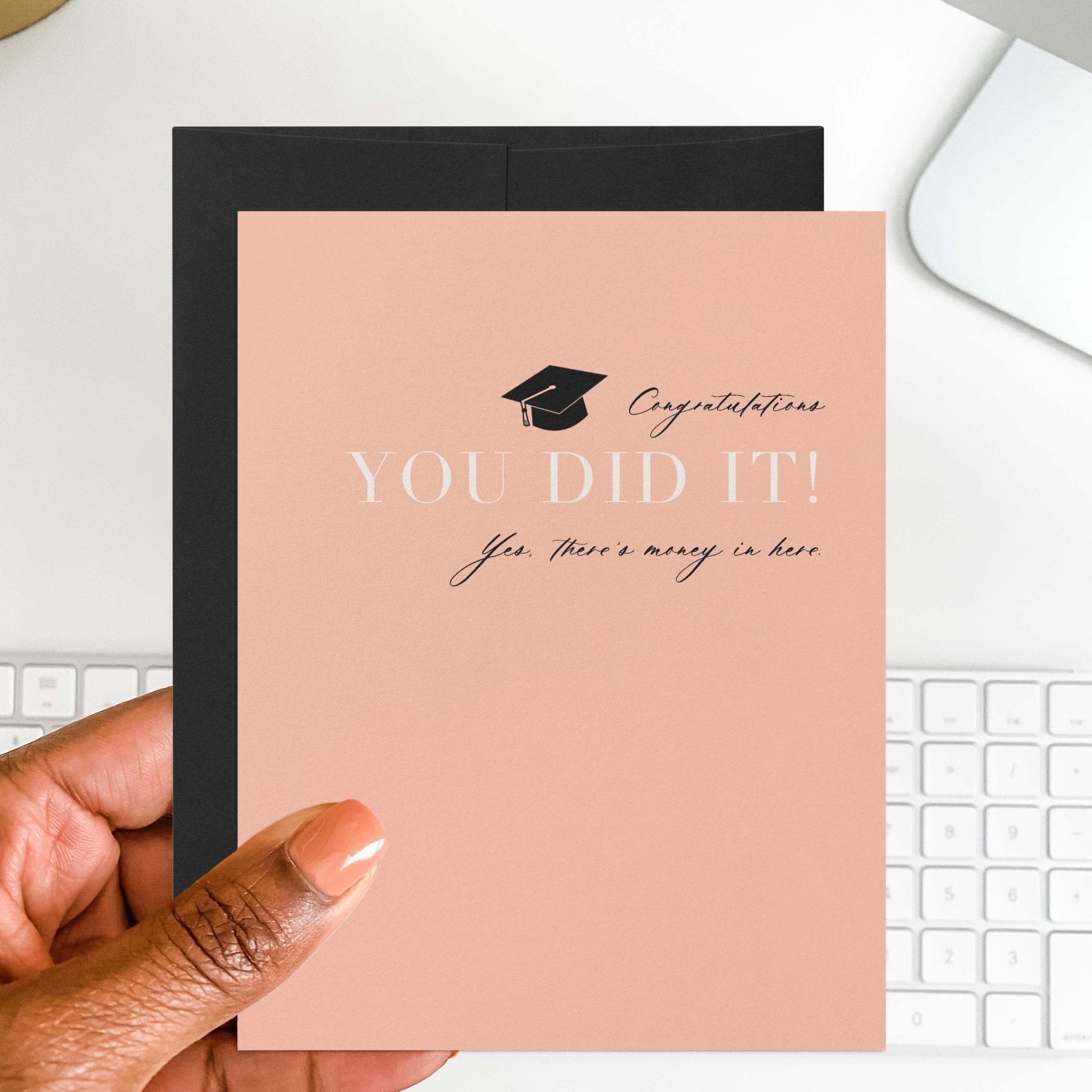 You Did It graduation card by Blú Rose held in hand over a white desk with keyboard and black envelope