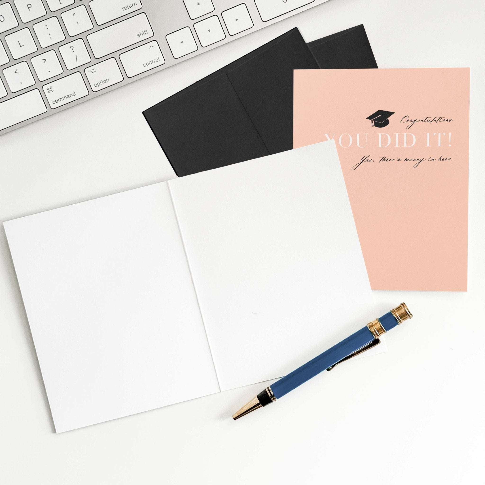 You Did It graduation money card by Blú Rose shown open with blank interior, black envelope and pen on a white desk