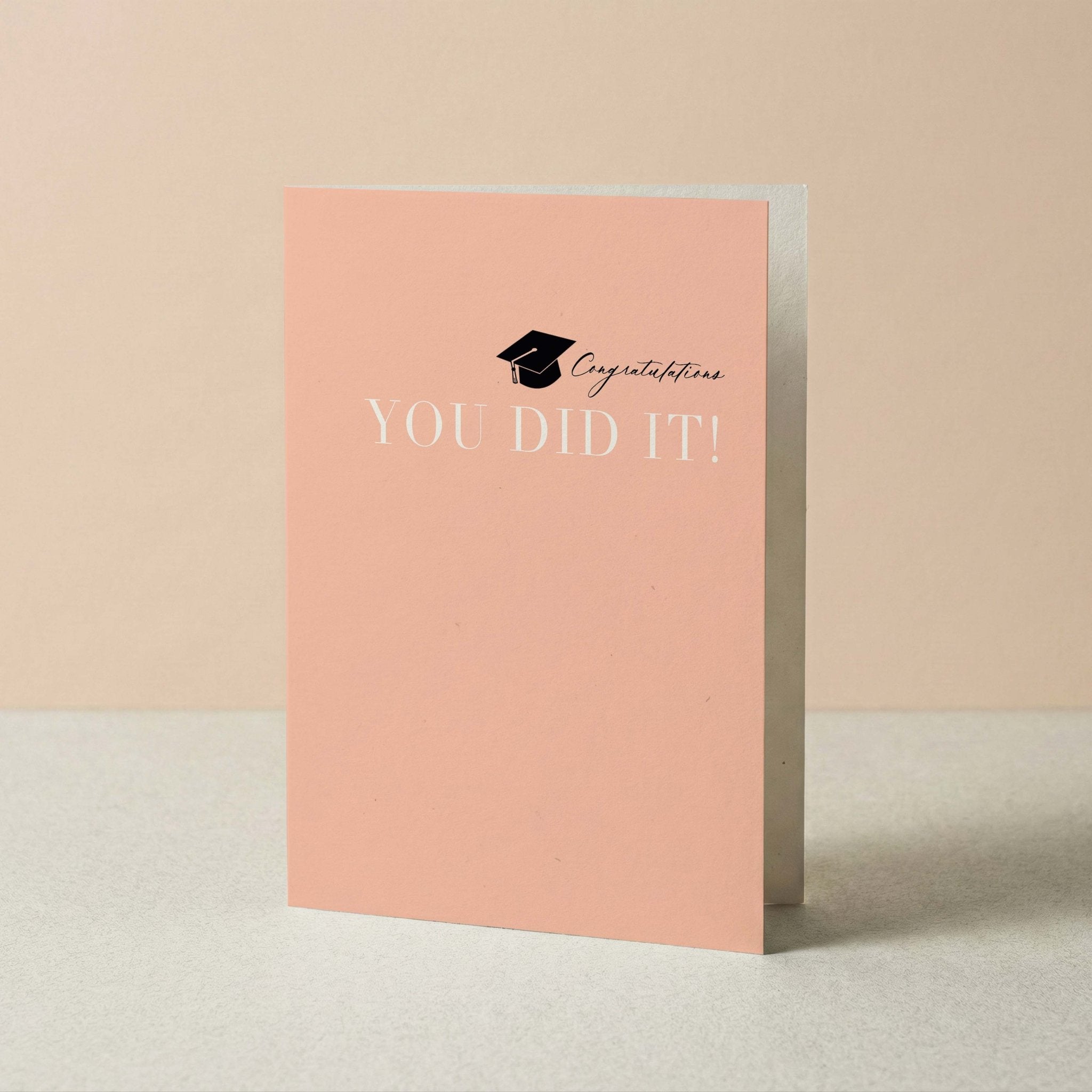 You Did It graduation card by Blú Rose standing upright, peach card with grad cap design on a neutral background