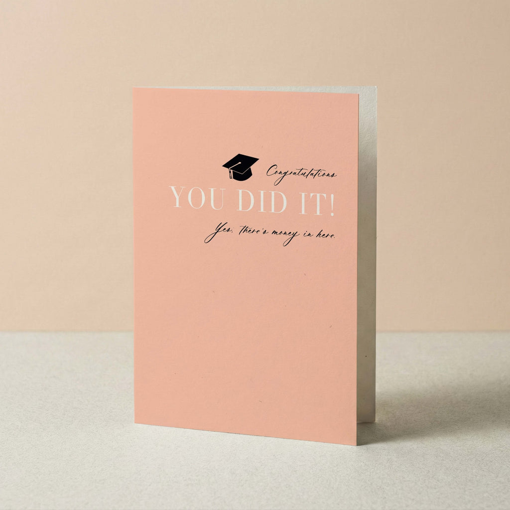 You Did It graduation card by Blú Rose standing upright, peach card with grad cap design on a neutral background
