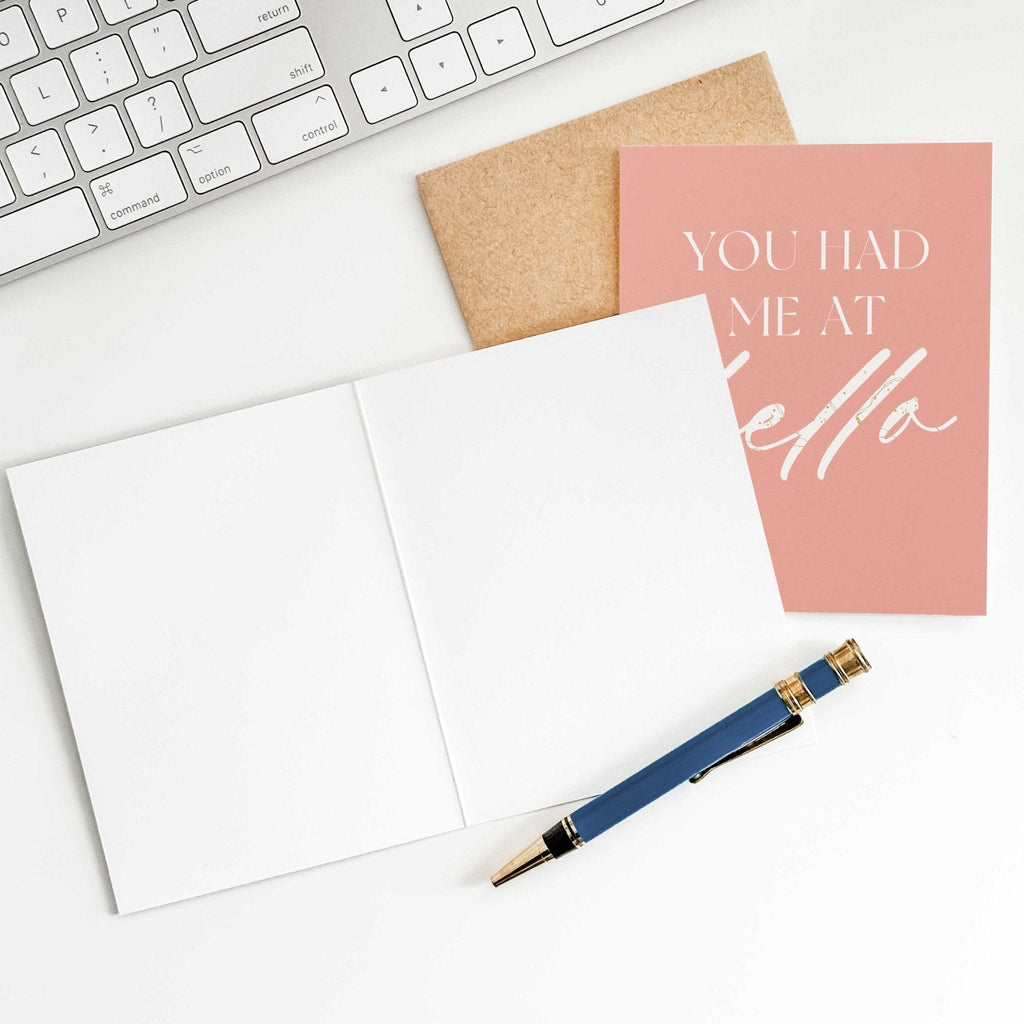 You Had Me at Hello love card by Blú Rose shown open with blank interior, kraft envelope and pen on a white desk