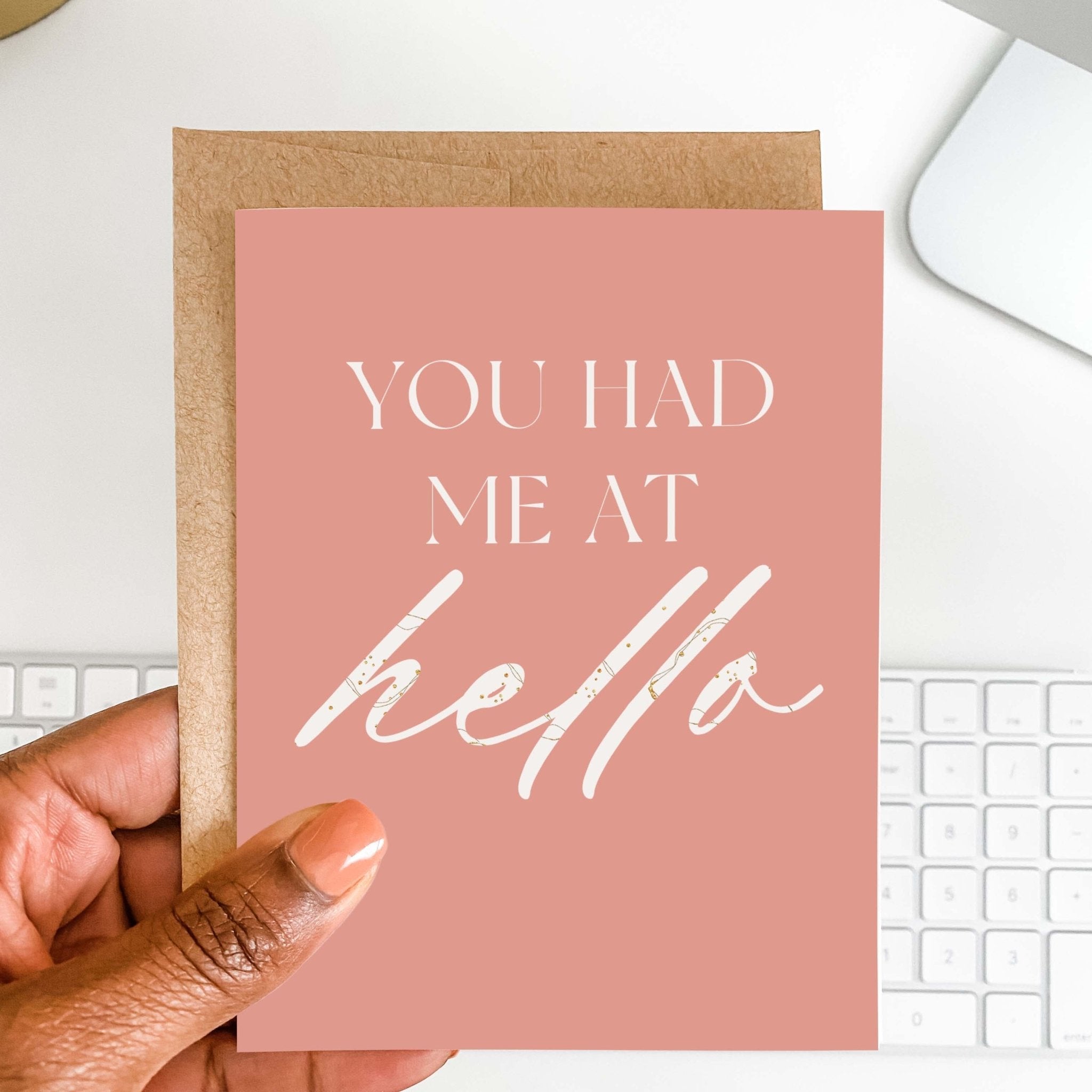 You Had Me at Hello romantic card by Blú Rose held in hand over a white desk with keyboard and kraft envelope