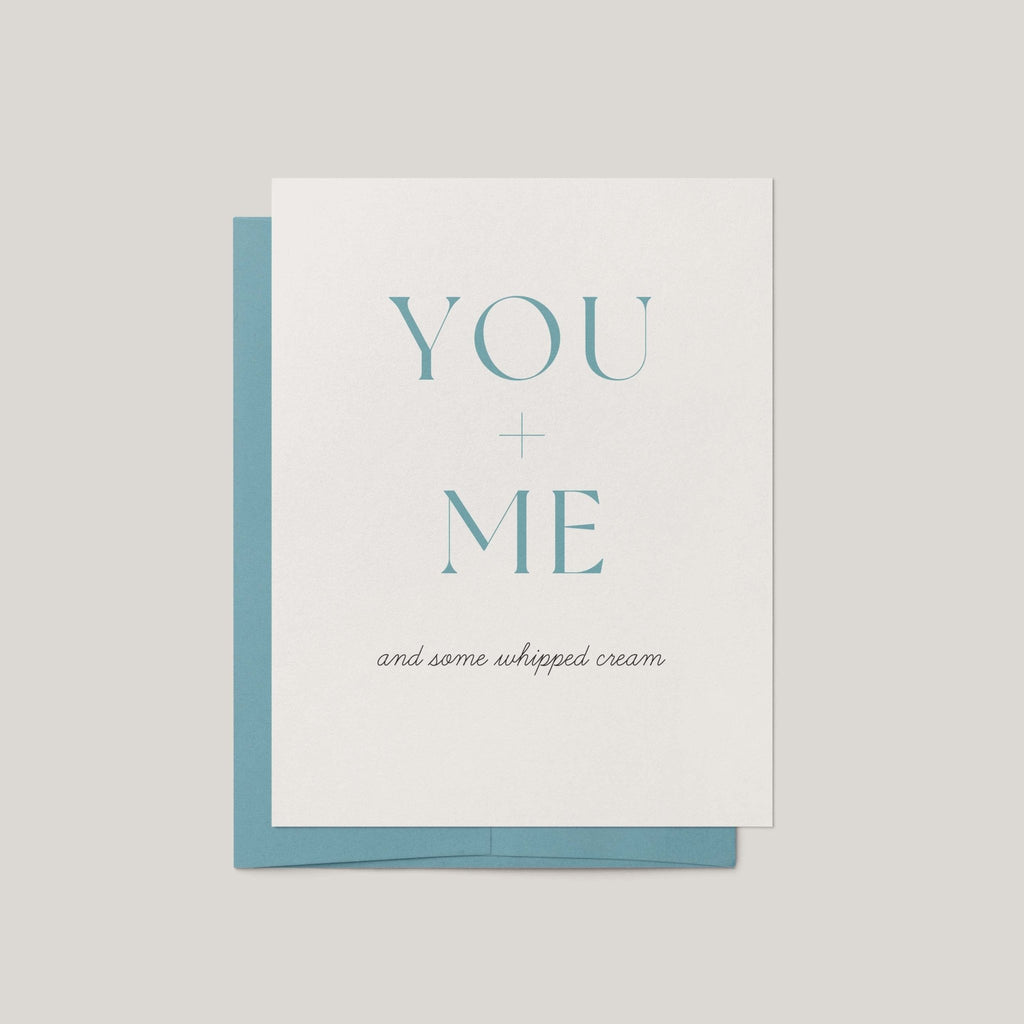 A greeting card with a white front and a light blue envelope behind it, printed with the words 'YOU + ME and some whipped cream' in pale blue and black text on a light gray background.