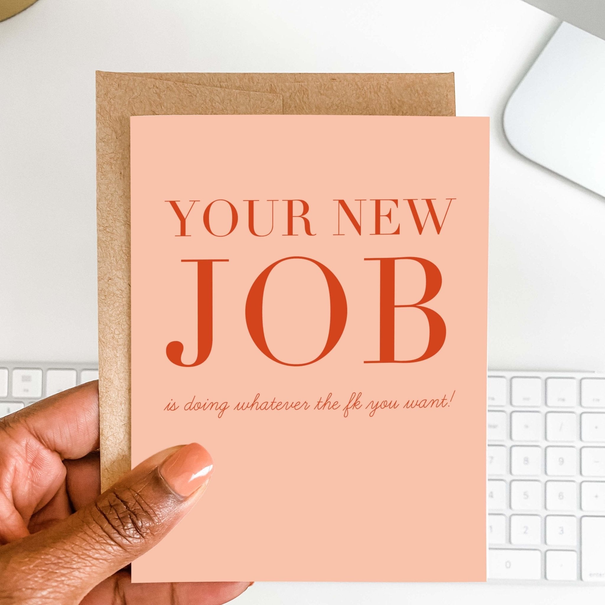 Your New Job Is funny retirement card by Blú Rose held in hand over a white desk with keyboard and kraft envelope
