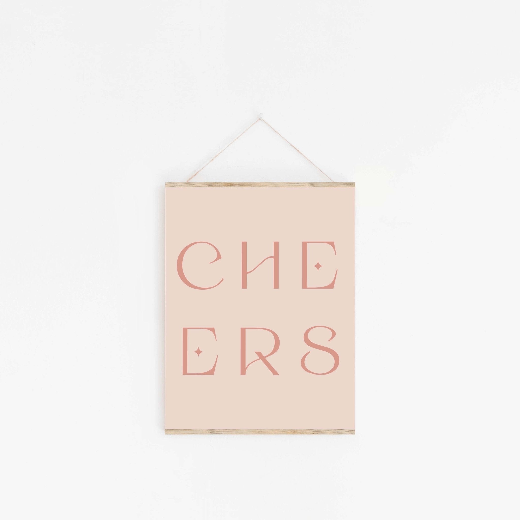 Pastel pink “CHEERS” typography art print hanging on white wall.