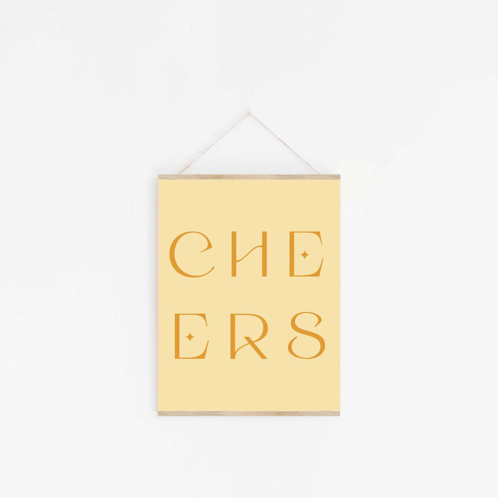 Pastel yellow “CHEERS” typography art print hanging on white wall.