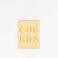 Pastel yellow “CHEERS” typography art print hanging on white wall.