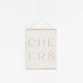 Beige “CHEERS” typography art print hung on a white wall.