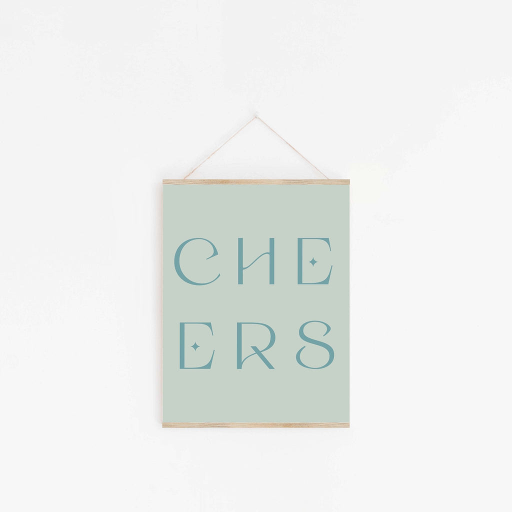 Pastel sage green “CHEERS” typography art print hanging on white wall.