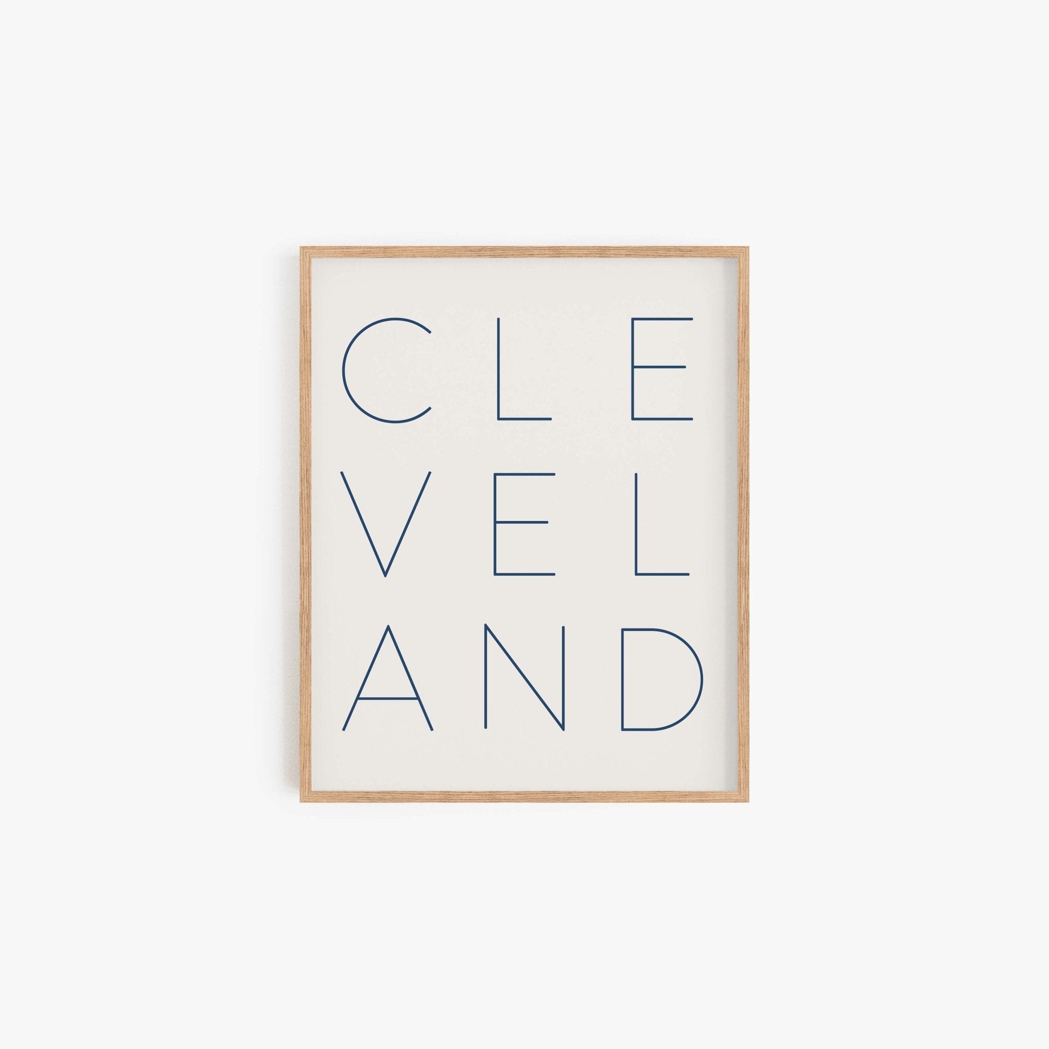 Minimalist Cleveland typography art print in navy lettering on off-white background in wood frame